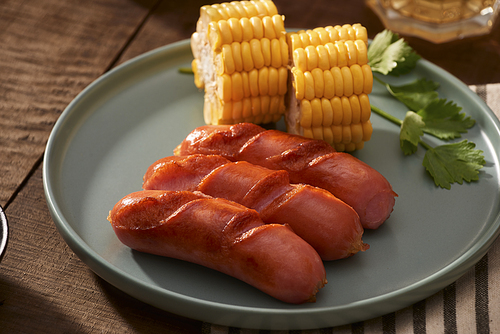 Home grilled sausages on a dark plate, a meat dish on a dark wooden background, hot sausages with spices and salt in a home kitchen, copy space, rustic style, art