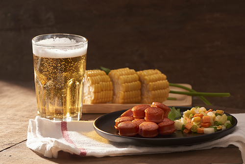 Grilled sausages with glass of beer on wooden table with copy space.