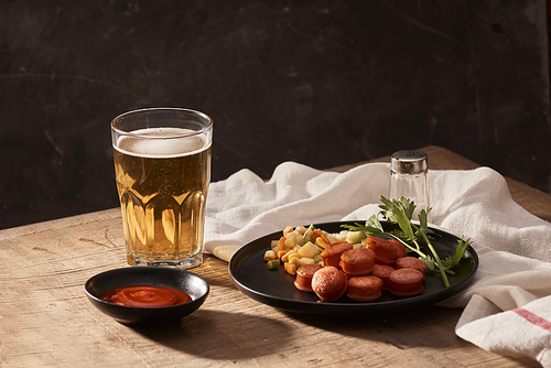 Glass of delicious beer with grilled sausages on wooden table