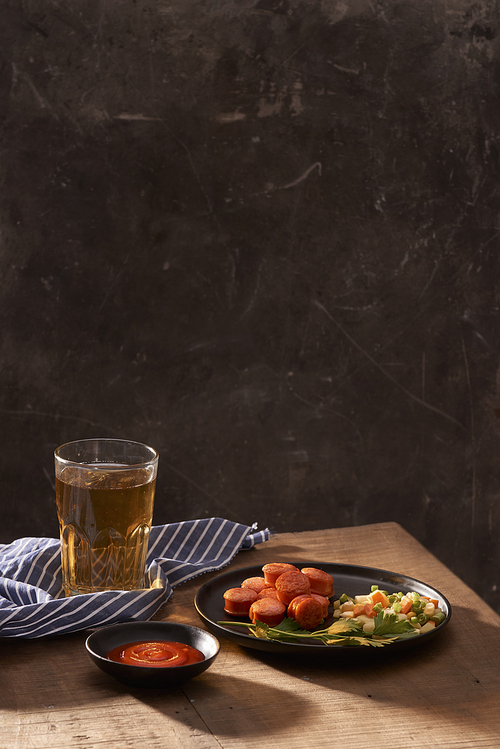 Glass of delicious beer with grilled sausages on wooden table