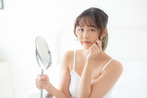 Beautiful young asian woman looking the mirror with acne problem at bedroom, trouble of beauty on face, zit treatment, asia girl is pimple having worry and displeased, skincare and healthy concept.