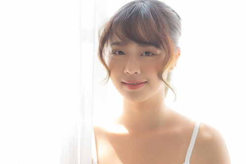 Portrait of beautiful young asian woman standing the window and smile while wake up with sunrise at morning, girl happy with freshness and cheerful, lifestyle and relax concept.