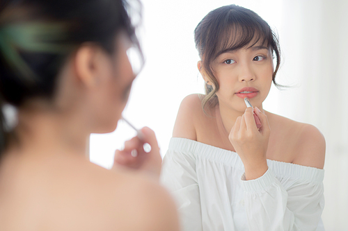 Beautiful portrait young asian woman looking mirror applying makeup lipstick at room, beauty lips asia girl makeup and cosmetic fashion on mouth at home, lifestyle and health care concept.