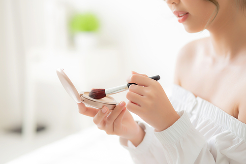 Beauty portrait young asian woman smiling with face looking mirror applying makeup with brush cheek in the bedroom, beautiful girl holding blusher facial, skin care and cosmetic concept.