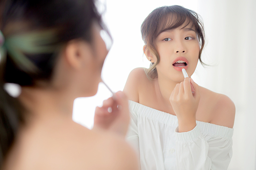 Beautiful portrait young asian woman looking mirror applying makeup lipstick at room, beauty lips asia girl makeup and cosmetic fashion on mouth at home, lifestyle and health care concept.