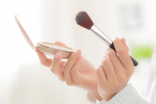 Closeup hand of beauty young asian woman with face looking mirror applying makeup with brush cheek in the bedroom, beautiful girl holding blusher facial, skin care and cosmetic concept.