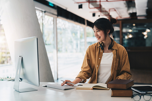 Hipster asian girl school student with wear headphone write notes watch video online webinar learn on laptop sit in bed distance elearning course video conference pc call in bedroom at home.