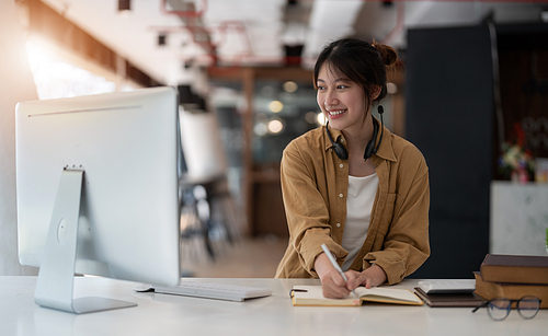 Smiling Asian young female using headset looking at laptop screen listen and learning online courses. Happy business woman with headphones video call for customer service.