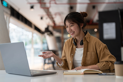 Portrait of young asian woman using laptop and writing making list taking notes in notepad working or learning on laptop indoors- educational course or training, seminar, education online concept