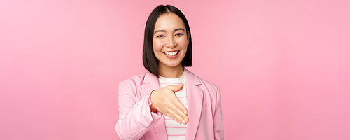 Portrait of smiling, pleasant businesswoman shaking hands with business partner, handshake, extending hand and saying hello, standing over pink background.