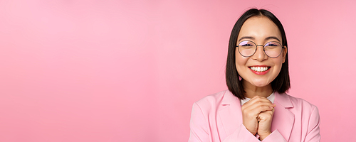 Close up portrait of smiling happy businesswoman in glasses, clench hands together thankful, excited of smth, begging or say please, standing over pink background.