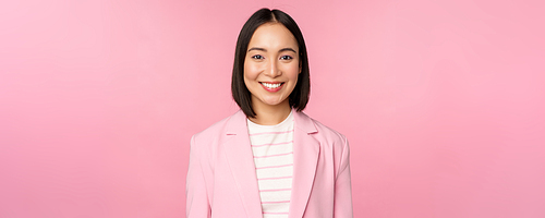 Young professionals. Smiling asian businesswoman, saleswoman in suit looking confident at camera, posing against pink background.