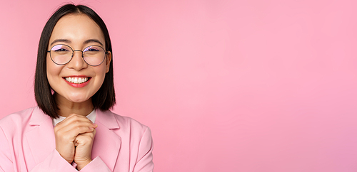 Close up portrait of smiling happy businesswoman in glasses, clench hands together thankful, excited of smth, begging or say please, standing over pink background.