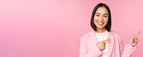 Enthusiastic professional businesswoman, saleswoman pointing fingers right, showing advertisement or company logo aside, posing over pink background.