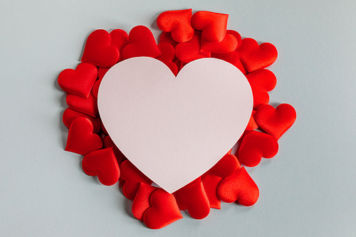 Valentine's day many red silk hearts and heart shaped white card on gray background, love concept