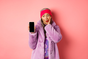 Valentines day shopping concept. Beautiful asian senior woman showing smartphone screen and looking at display excited, checking out online offer, pink background.