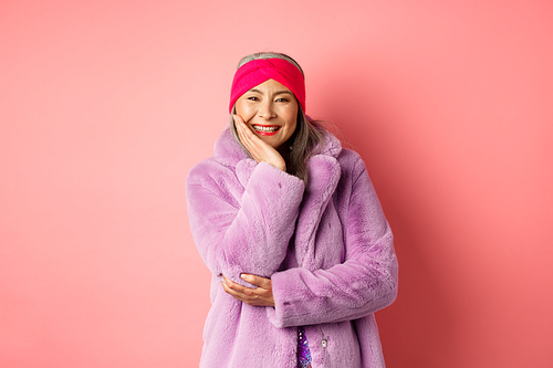 Fashion and shopping. Beautiful and romantic asian mature woman looking caring and heartfelt at camera, smiling happy, standing over pink background.