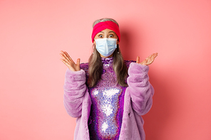 Covid-19, social distancing and fashion concept. Surprised asian senior woman in stylish outfit and respirator checking out awesome promo, spread hands and staring at camera amazed.