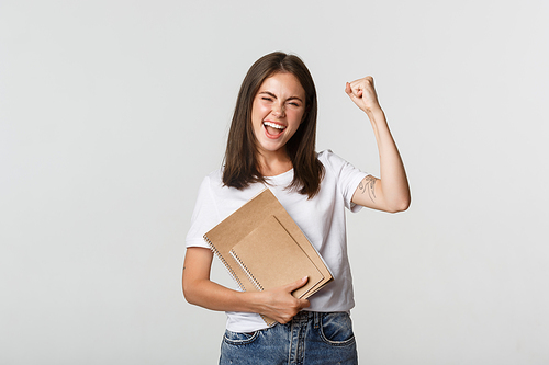 Rejoicing smiling woman holding notebooks and fist pump cheerful, celebrating.