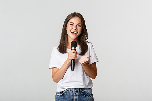 Beautiful young woman singing song in microphone at karaoke, standing white background.