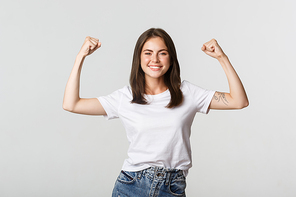 Portrait of confident attractive girl flex biceps to show strengths, smiling sassy.