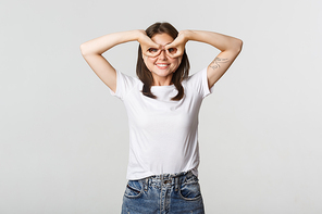 Cheerful good-looking young girl making superhero mask with hands over eyes and smiling happy.