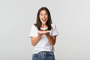 Excited attractive brunette b-day girl making wish on birthday cake, white background.