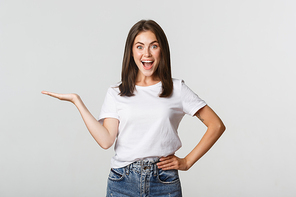 Excited beautiful girl extend arm, holding something on hand and looking happy.