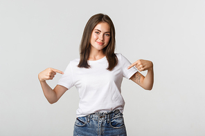 Beautiful smiling brunette girl pointing fingers at your logo, showing something on center.