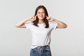 Annoyed brunette girl grimacing, shut ears with fingers from loud noise.