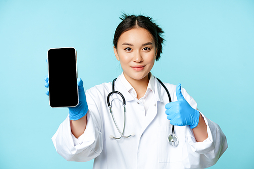 Web healthcare, online help concept. Confident asian female doctor or nurse, showing smartphone screen, app interface and thumbs up, recommending website.