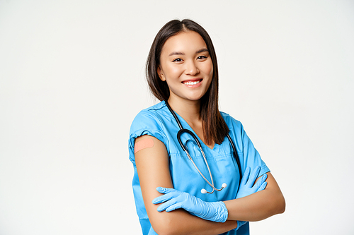 Smiling nurse, healthcare worker cross arms on chest, showing arm with patch, use vaccine shot from covid-19, standing over white background.