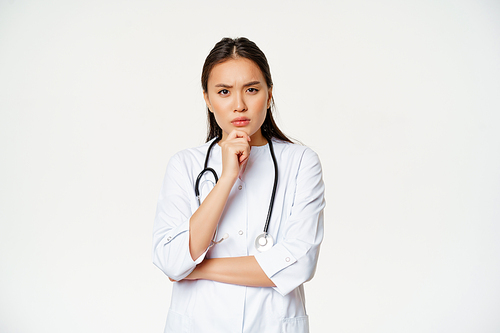 Asian female doctor in uniform thinking, looking serious and concerned, touching chin while pondering, listening patient at hospital, white background.