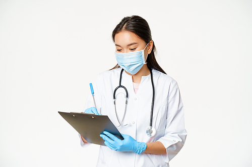 Female asian physician writing down patient info on clipboard, write prescription or diagnose, standing in medical mask with rubber gloves, white background.