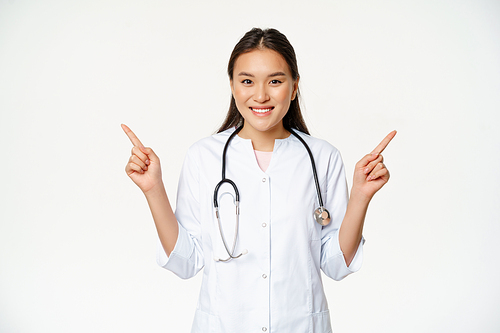 Smiling professional physician in white robe, pointing fingers sideways and showing two advertisements, both ways, standing against white background.