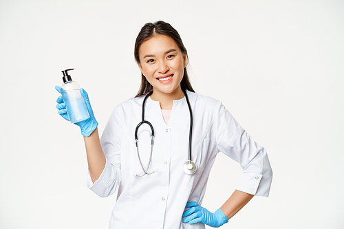 Smiling asian physician holding hand sanitizer in rubber gloves, showing bottle with antiseptic for coronavirus prevention, white background.