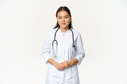 Smiling asian medical worker with stethoscope, wearing doctor uniform, looking helpful at patient, standing over white background.