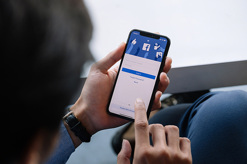 CHIANG MAI, THAILAND - JAN 17, 2021: Facebook social media app logo on log-in, sign-up registration page on mobile app screen on iPhone X (10) in person's hand working on e-commerce shopping business