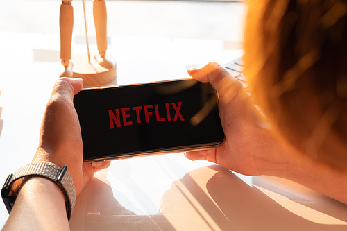 CHIANG MAI, THAILAND - DEC.14 ,2019 : Young woman using iphone xs using Netflix in her smartphone. Millennial girl resting with her cell phone in her hands and the Netflix logo in the screen.