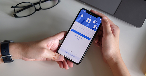 CHIANG MAI ,THAILAND - JULY 3, 2020 : Woman hand holding iPhone X to use facebook with new login screen.Facebook is a largest social network and most popular social networking site in the world.