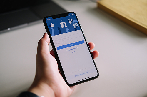 CHIANG MAI ,THAILAND - JULY 3, 2020 : Woman hand holding iPhone X to use facebook with login screen.Facebook is a largest social network and most popular social networking site in the world.