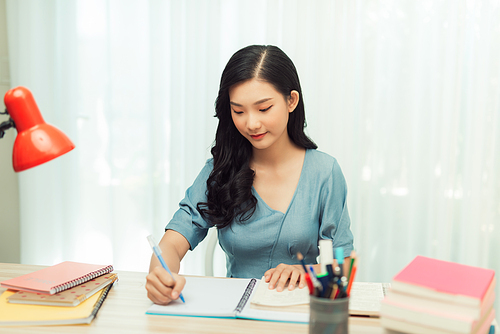 Concentrated young Asian female student sitting at desk at home