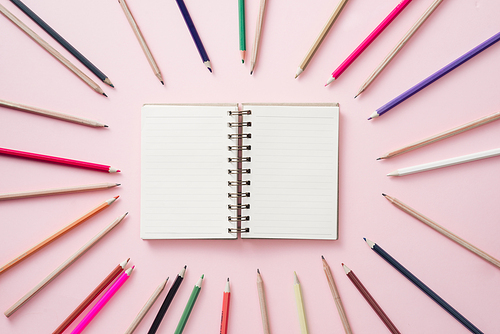 Notebooks in center with Bright colored pencils lined around the perimeter of the pink background.