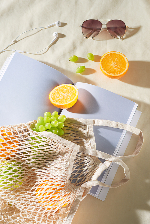 Summer holiday with fruit bag, glasses, earphone and magazine on light background.