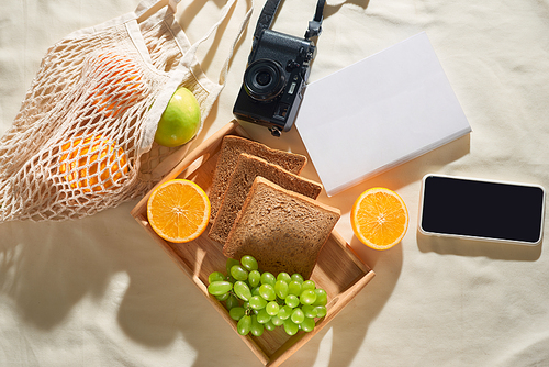 Summer holiday, gadget, fruit, camera, juice on light fabric background. Picnic concept.