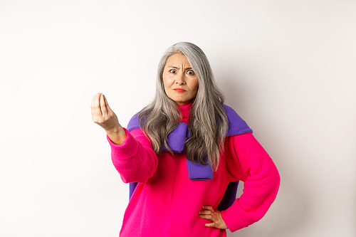 Funny asian woman staring angry and confused, shaking fingers, standing grumpy against white background. Copy space