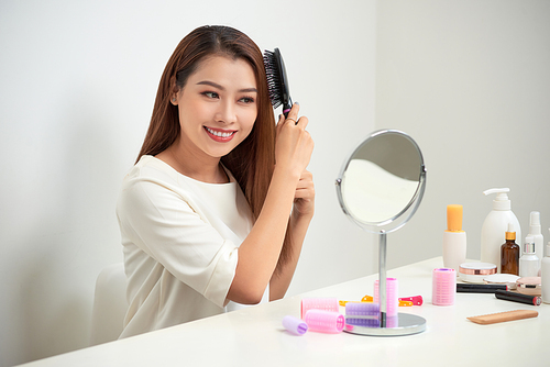 Getting rid of tangles. Beautiful young woman looking at her reflection in mirrorand brushing her long hair while sitting at the dressing table