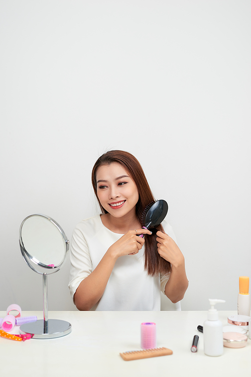 Getting rid of tangles. Beautiful young woman looking at her reflection in mirrorand brushing her long hair while sitting at the dressing table