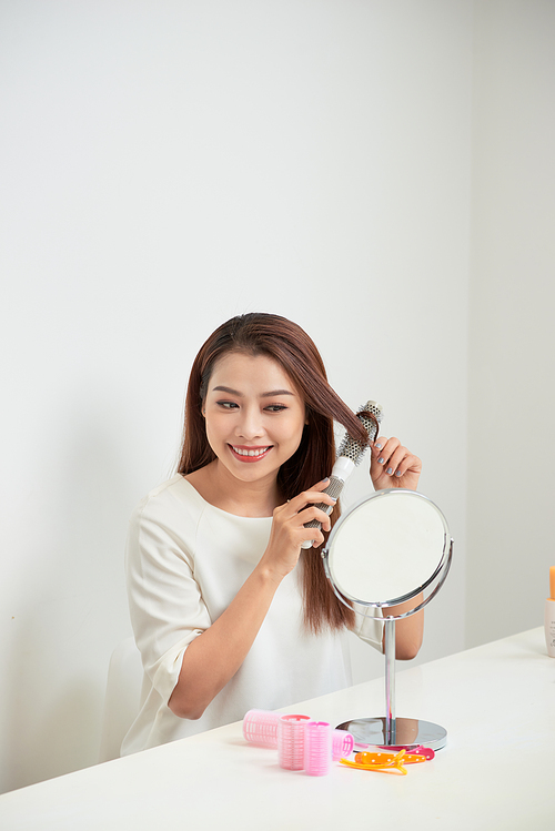 Getting rid of tangles. Beautiful young woman looking at her reflection in mirrorand brushing her long hair while sitting at the dressing table