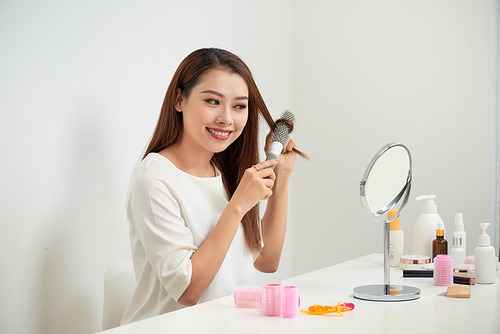 Getting rid of tangles. Beautiful young woman looking at her reflection in mirrorand brushing her long hair while sitting at the dressing table